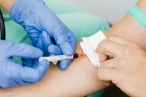 A gloved healthcare professional draws a blood sample from a patient's arm using a syringe.