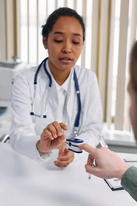 A doctor in scrubs checks a patient's finger with a pulse oximeter during a routine check-up.