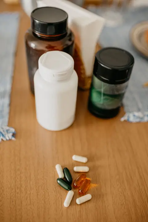 Assorted supplement bottles and loose capsules arranged on a wooden table.