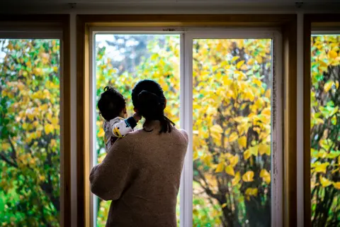 a mother holds her child while gazing out a window, a wistful, reflective moment