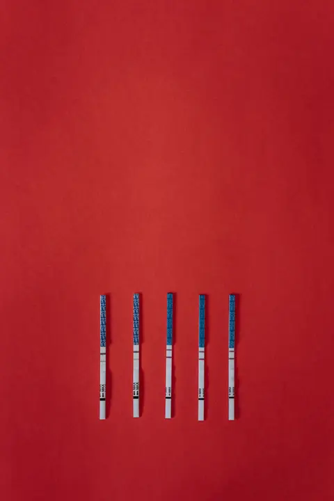 Five HCG/LH-style test strips with faint positive lines laid out flat against a bold red background.
