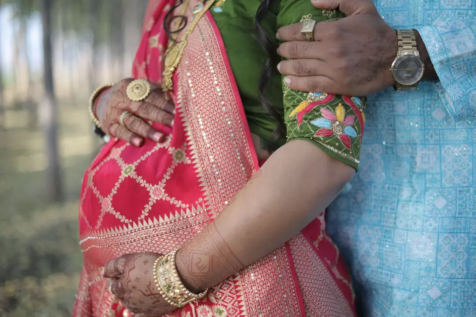 Close-up of a pregnant woman's belly in a pink sari, her hand and her partner's hand both resting on it