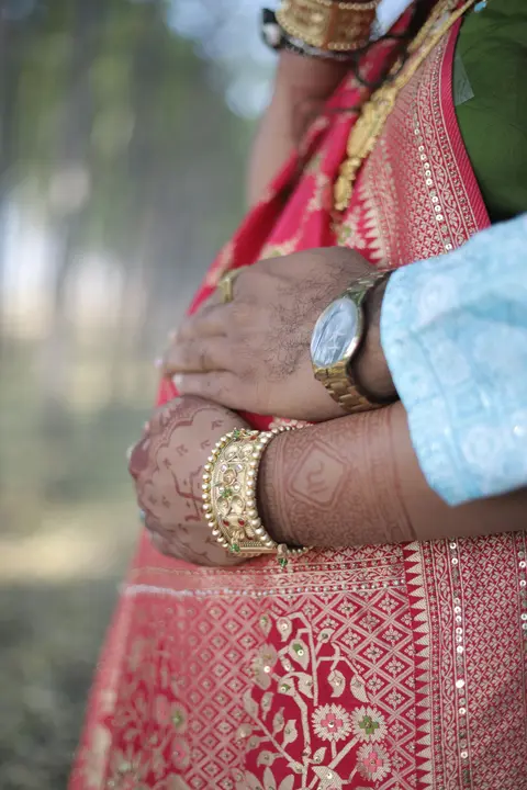 Close-up of a pregnant woman's henna-decorated hands resting on her belly, wearing gold bangles and a red-and-gold sari