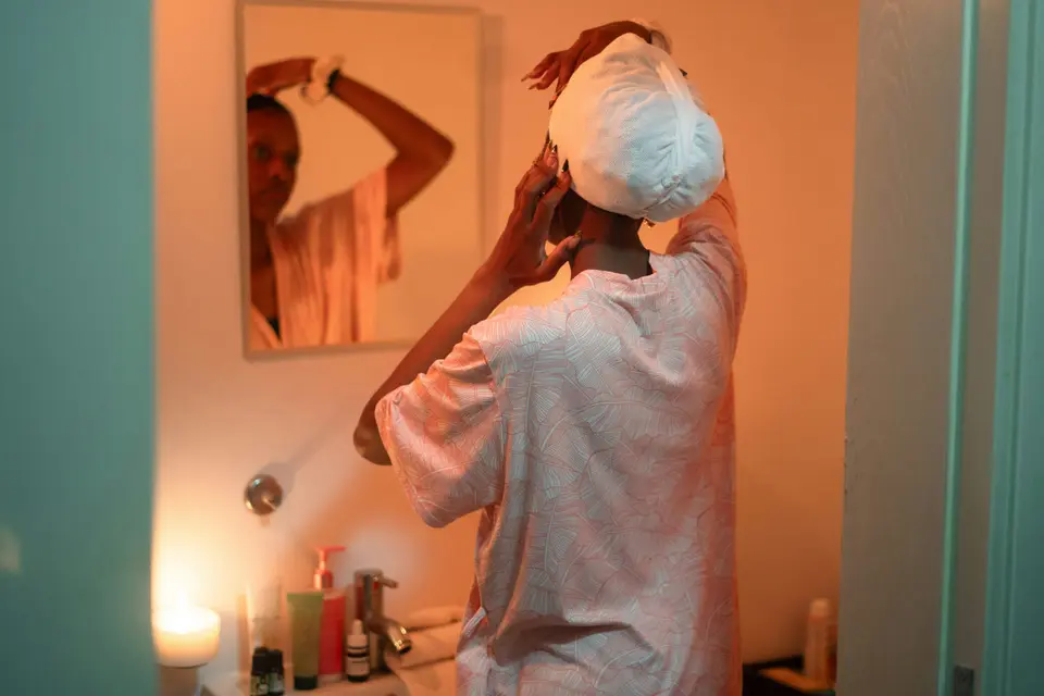 a woman gently towel-dries and tends to her hair while looking in a bathroom mirror