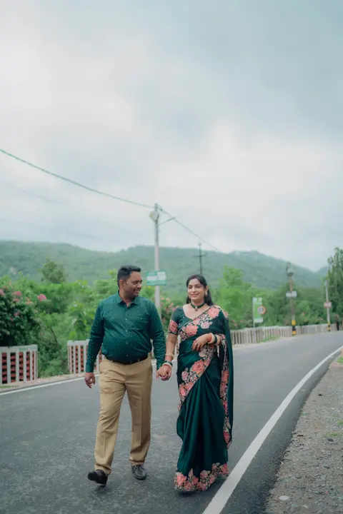 an Indian husband and wife in traditional dress walk together hand in hand smiling on a country road