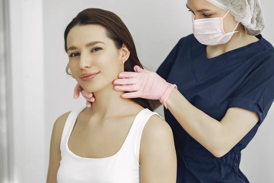 A clinician in gloves gently examines a smiling woman's neck during a routine check-up.