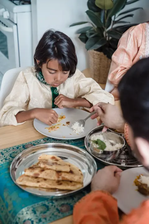 A South Asian family shares a home-cooked meal of roti, rice and curry at the table, with a child feeding himself from his own plate.