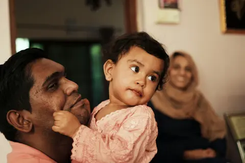 a South Asian relative holds a baby at a warm evening family gathering