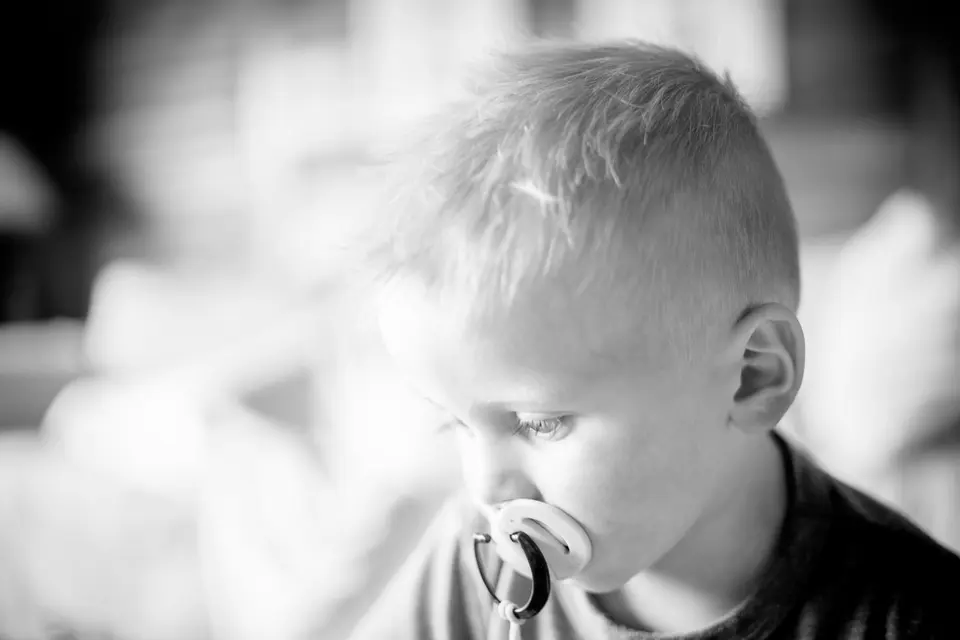 A close-up black-and-white portrait of a toddler boy with a pacifier in his mouth.